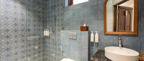 A bathroom with a patterned tile wall, a freestanding bathtub, a sink with a wooden countertop, and a mirror with an arched frame.