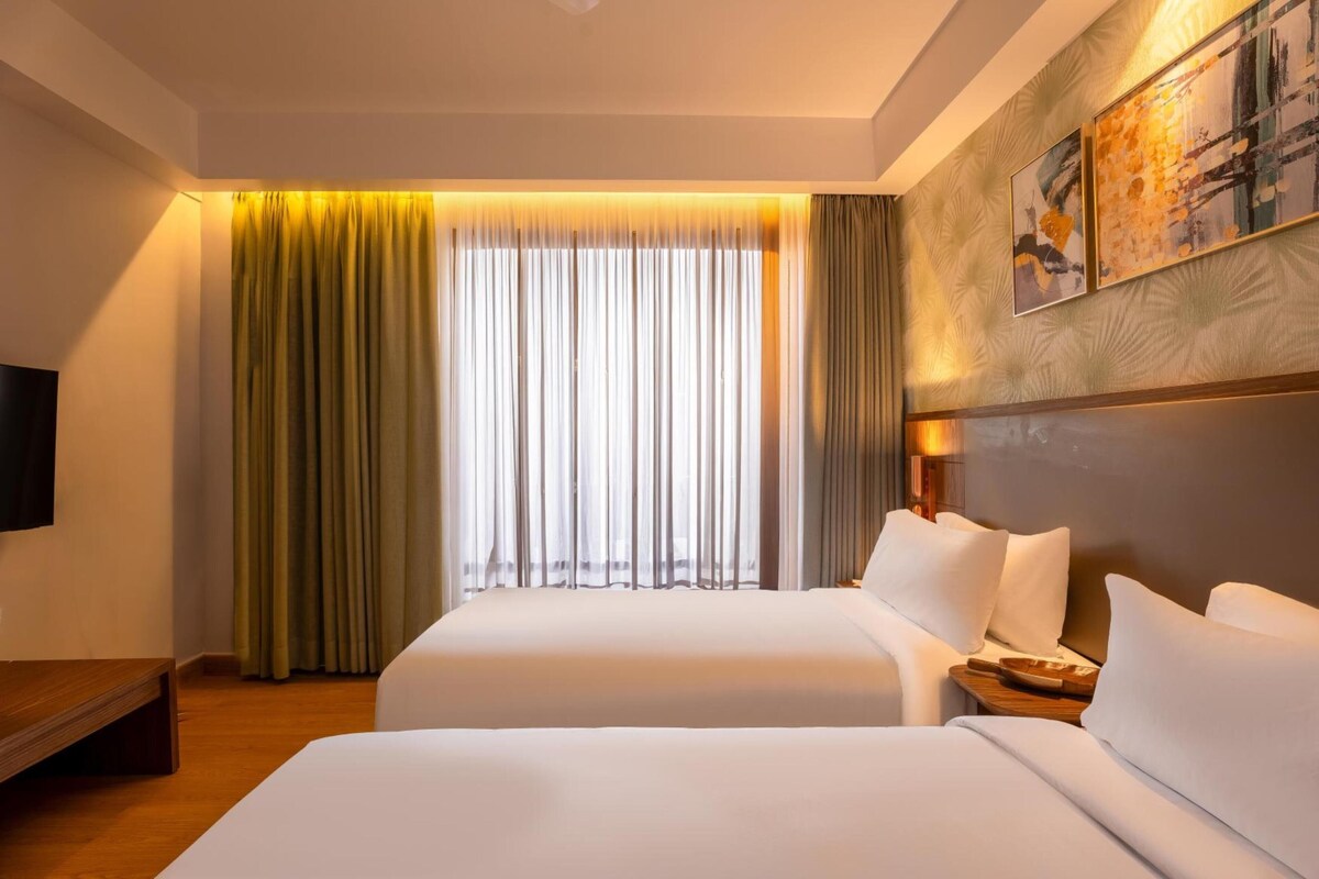 A hotel room with two beds, a flat-screen TV, a wooden nightstand, and a large window with curtains.