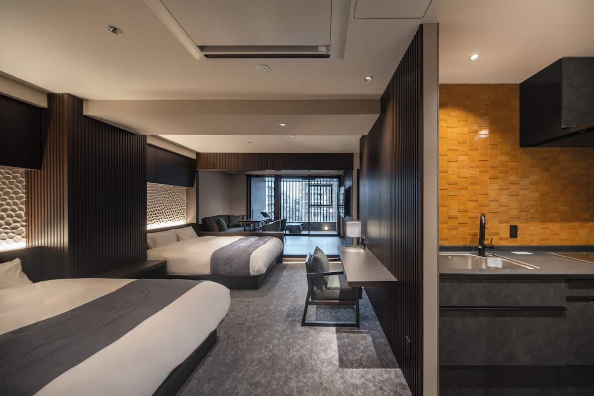 Ein modernes Hotelzimmer mit einem großen Bett, einem Schreibtisch, einem Sessel, einer Couch, einem kleinen Tisch, einem Fenster und einer Küchenzeile.