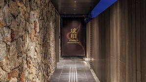 A corridor with a stone wall on one side and a wooden wall on the other, leading to a sign with 'Kohaku' and 'APARTMENT HOTEL KYOTO' written on it. - KOHAKU Apartment Hotel Kyoto (Kyoto)