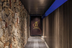 A corridor with a stone wall on one side and a wooden wall on the other, leading to a sign with 'Kohaku' and 'APARTMENT HOTEL KYOTO' written on it. - KOHAKU Apartment Hotel Kyoto (Kyoto)