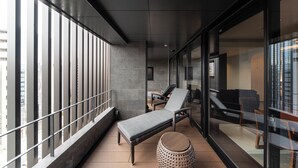 A balcony with a lounge chair, a small round table, and a view of the cityscape through large windows. - KOHAKU Apartment Hotel Kyoto (Kyoto)