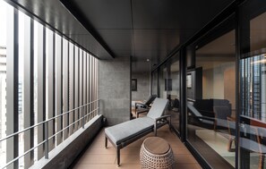 A balcony with a lounge chair, a small round table, and a view of the cityscape through large windows. - KOHAKU Apartment Hotel Kyoto (Kyoto)