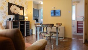 A living room with a sofa, a dining table with chairs, a TV, and a kitchen area.