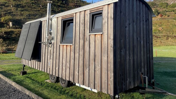 A wooden RV with a sliding door, windows, and a metal awning.