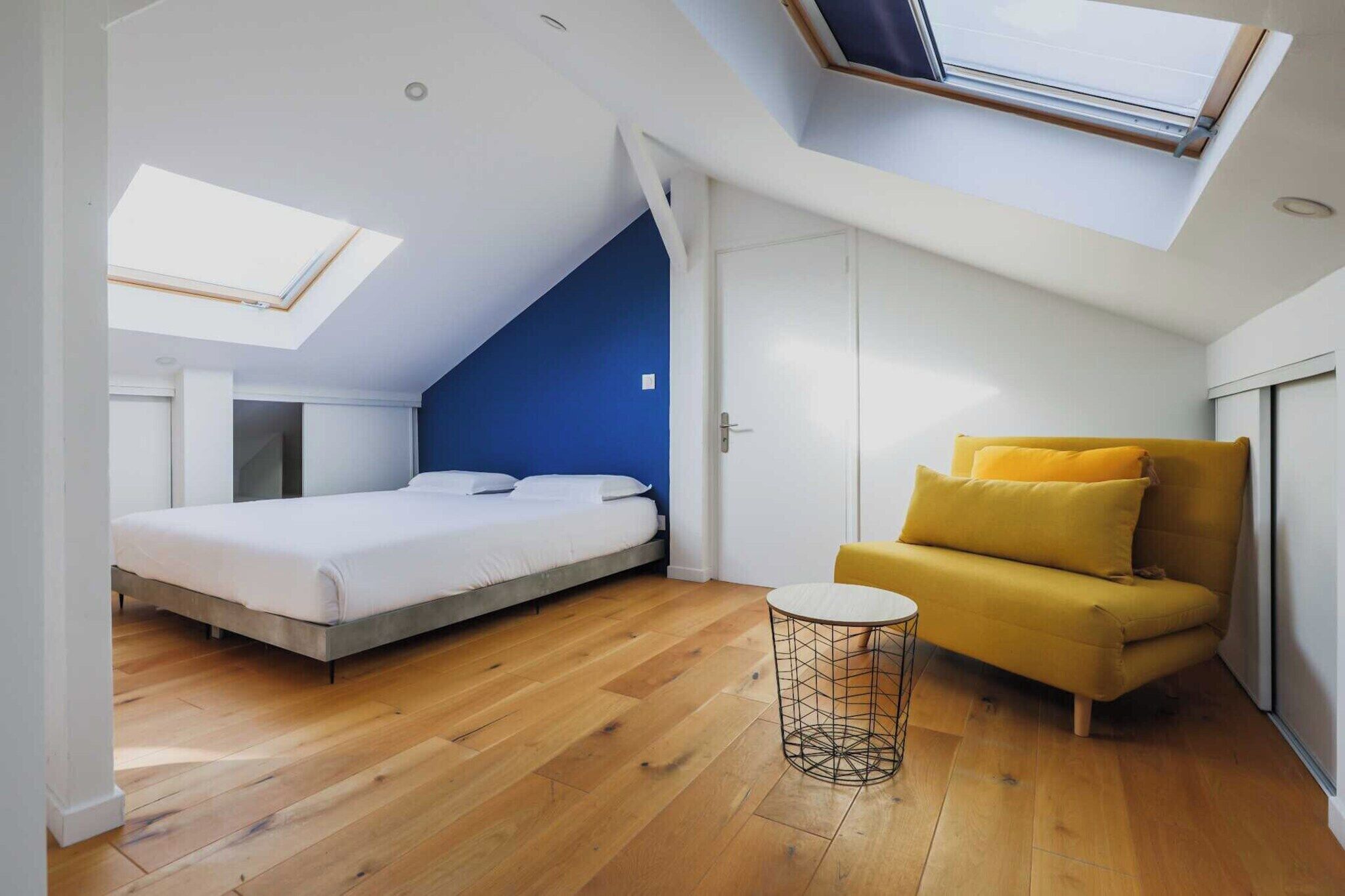 Une chambre avec une lucarne, un lit, un canapé et une petite table.