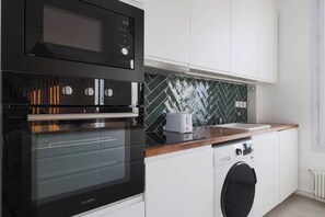 A compact kitchen with a black oven, a microwave, a toaster, and a washing machine. - Magnificent apartment -2BR-6P- Saint-Denis (Saint-Denis)