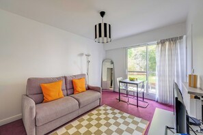 Ein Wohnzimmer mit einer Couch, einem Tisch, einem Stuhl, einem Fernseher und einem Fenster mit Vorhängen.