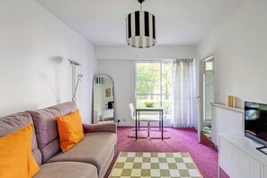 Ein Wohnzimmer mit einer Couch, einem Tisch mit Stühlen, einem Fernseher und einem Fenster mit Vorhängen.