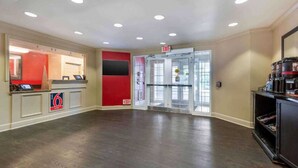 Spaziosa hall con reception, parete decorata in rosso e ingresso con porta in vetro.