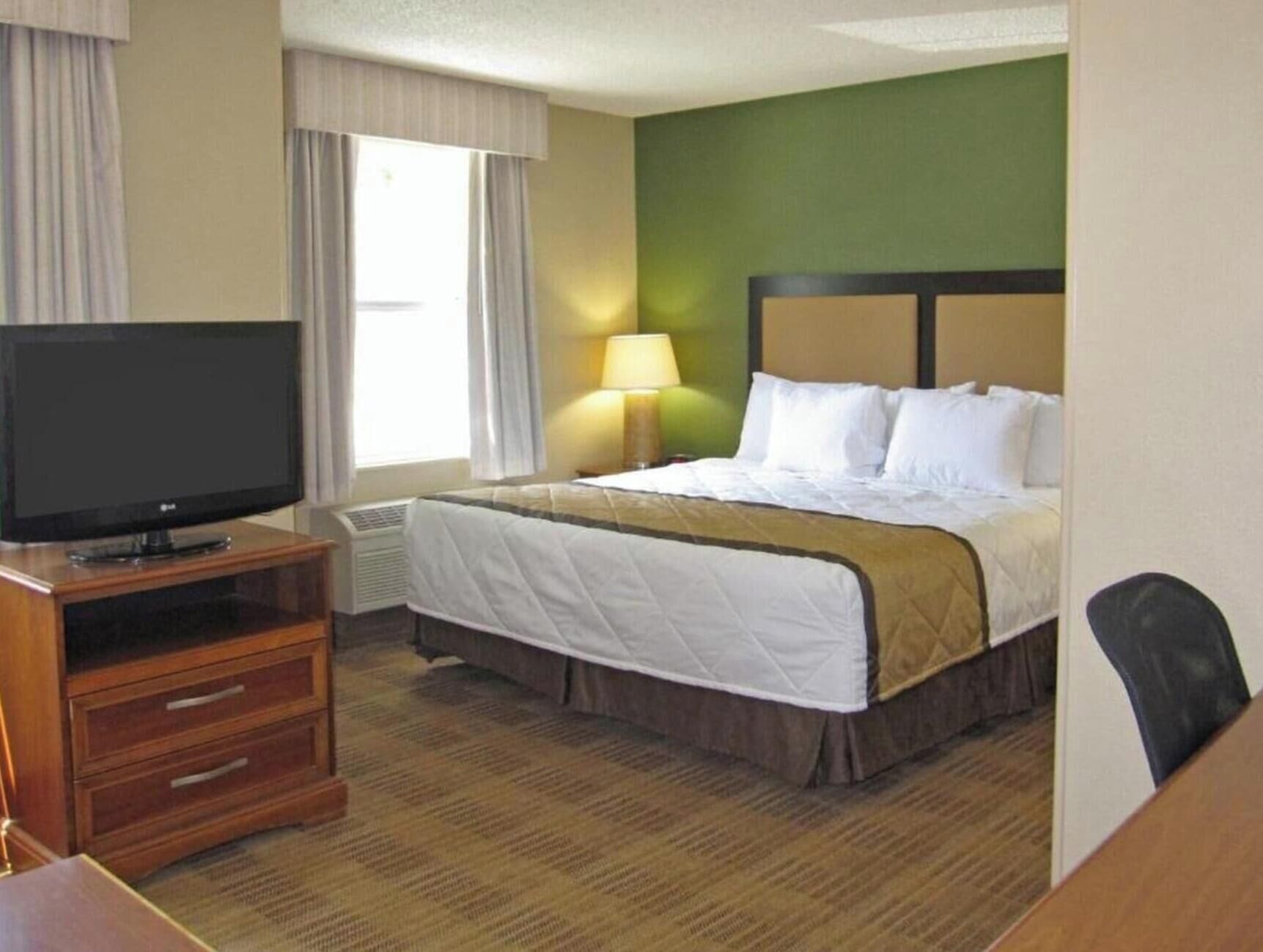 A hotel room with a bed, a television, a lamp, and a desk.