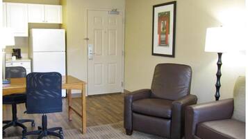 A hotel room with a kitchenette, a desk with a chair, a sofa, a chair, and a lamp.