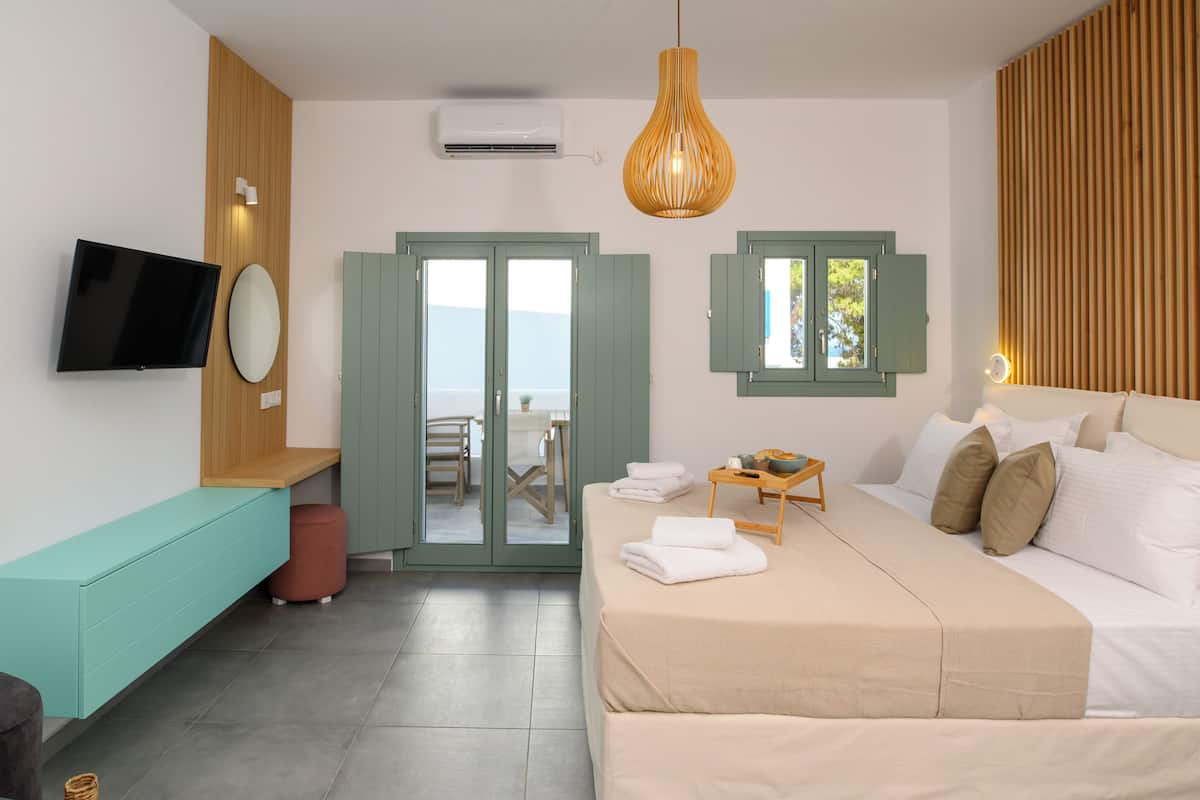 Quarto de hotel moderno com cama, televisão, área de estar e vista pela porta.