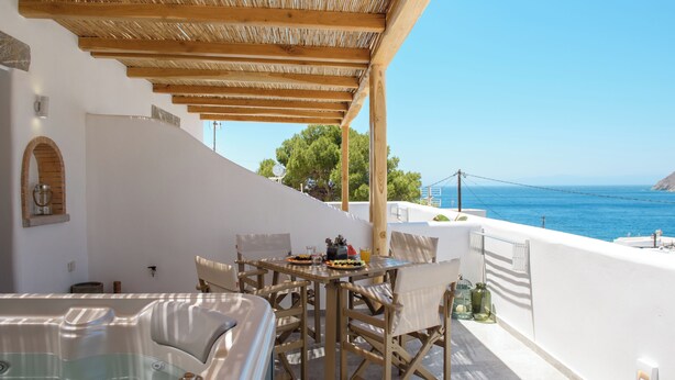 Une terrasse dotée d’un jacuzzi, d’une table à manger et de chaises, offrant une vue imprenable sur la côte.