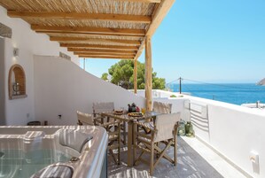 Una terraza con jacuzzi, mesa de comedor y sillas, con vistas a la costa.
