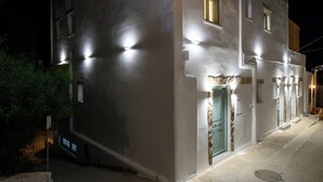 Un bâtiment doté de nombreuses fenêtres illuminées et d’une porte, le tout étant bordé d’une rue étroite.