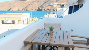 Une table et des chaises en bois sur un balcon donnant sur la mer et les bâtiments.