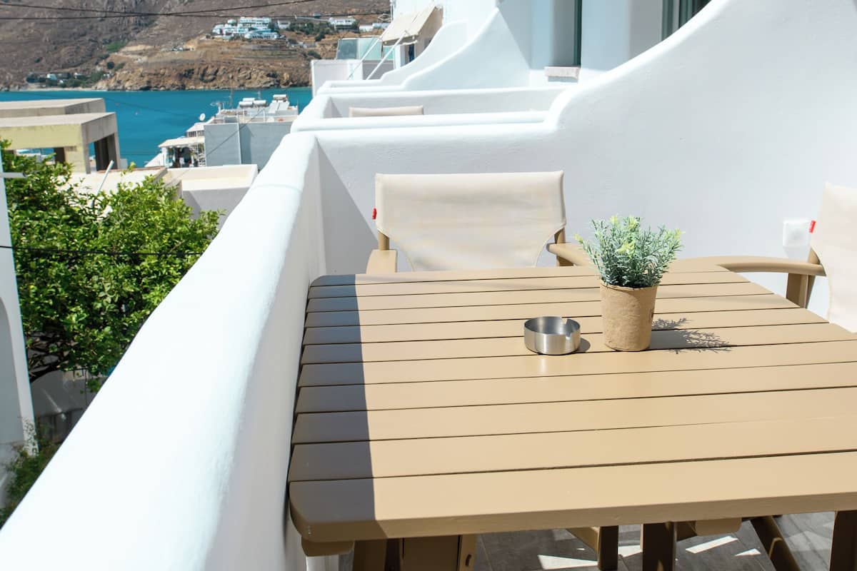 Uma varanda com mesa e cadeiras, um vaso de planta e vista para o mar e edifícios.