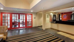 A hotel lobby with a reception desk, a red door with glass panels, and a striped carpet. - Studio6 Fishkill 2 Full Beds, Mobil Tub, Nsmk Kitchen (Fishkill)