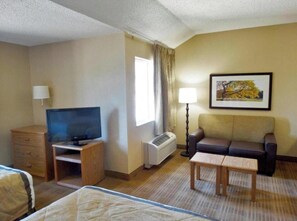 A hotel room with a bed, a desk with a television, a sofa, a small table, a lamp, and a framed picture on the wall. - Studio6 Fishkill 2 Full Beds, Mobil Tub, Nsmk Kitchen (Fishkill)