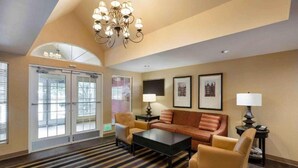 A hotel room with a sofa, armchairs, a coffee table, a chandelier, framed pictures on the wall, and a large window with blinds. - Studio6 Fishkill 2 Full Beds, Mobil Tub, Nsmk Kitchen (Fishkill)