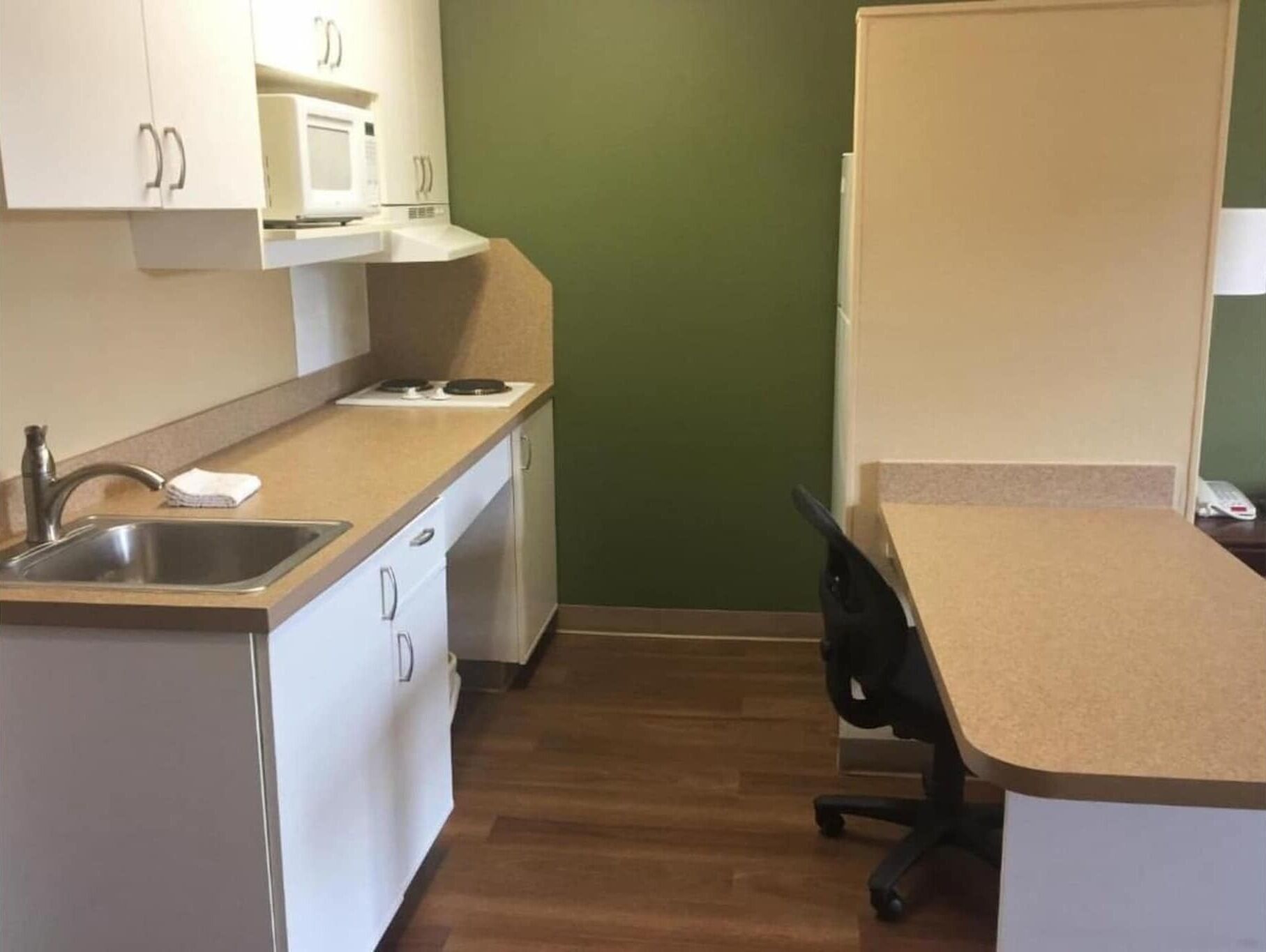 A compact kitchen with a microwave, stove, sink, and a small office desk.