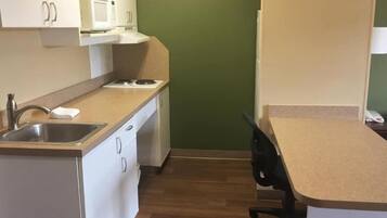 A compact kitchen with a microwave, stove, sink, and a small office desk.