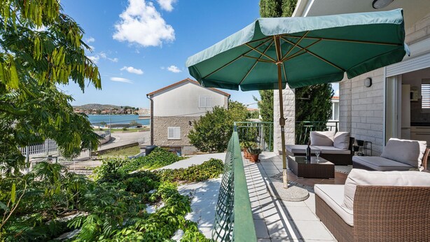 En balkon med udendørs møbler, en grøn parasol og havudsigt.