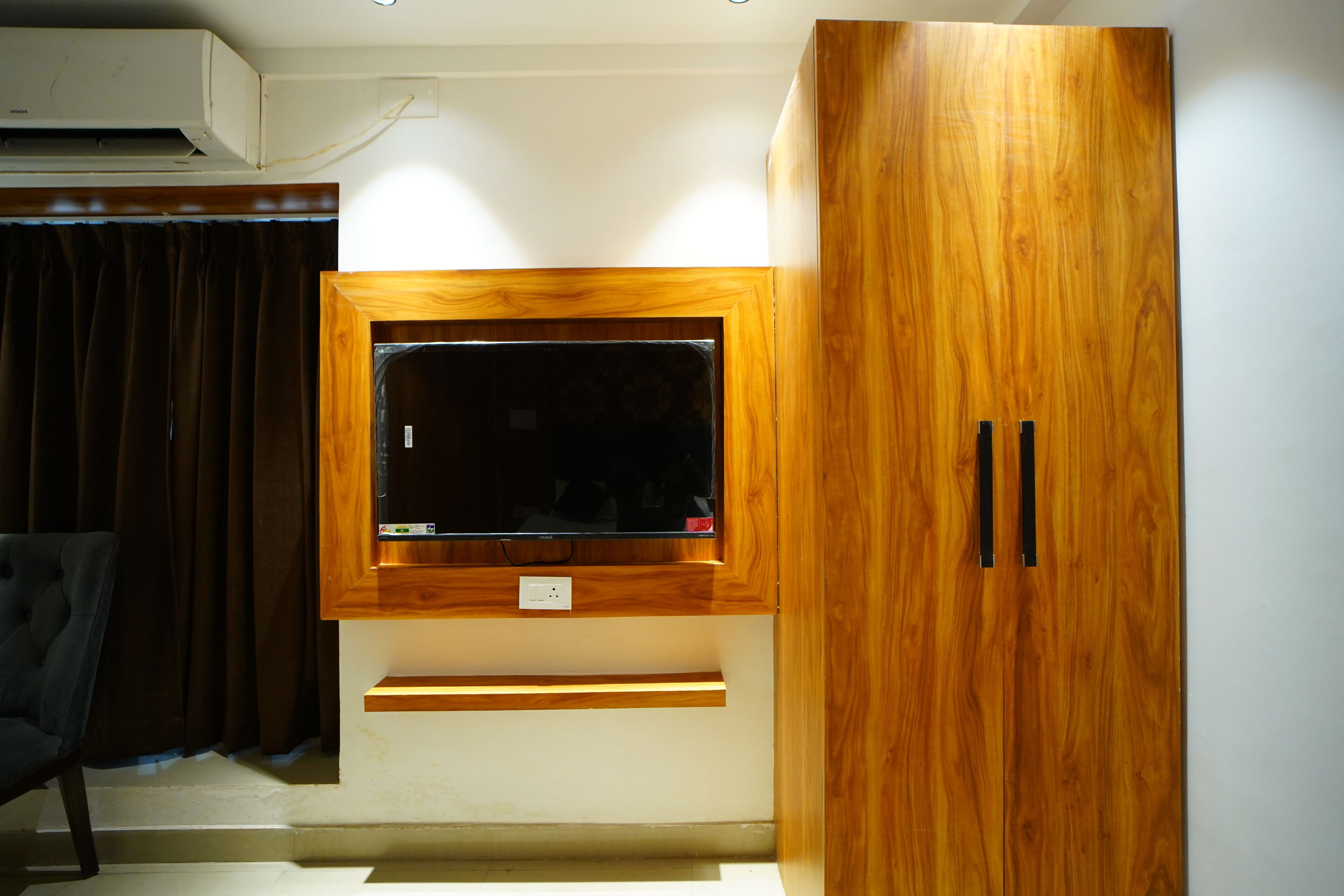 Una habitación con televisor montado, armario de madera y una silla.