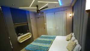 Una camera d'albergo moderna con un letto, una TV a muro, una ventola a soffitto e una finestra con tende.
