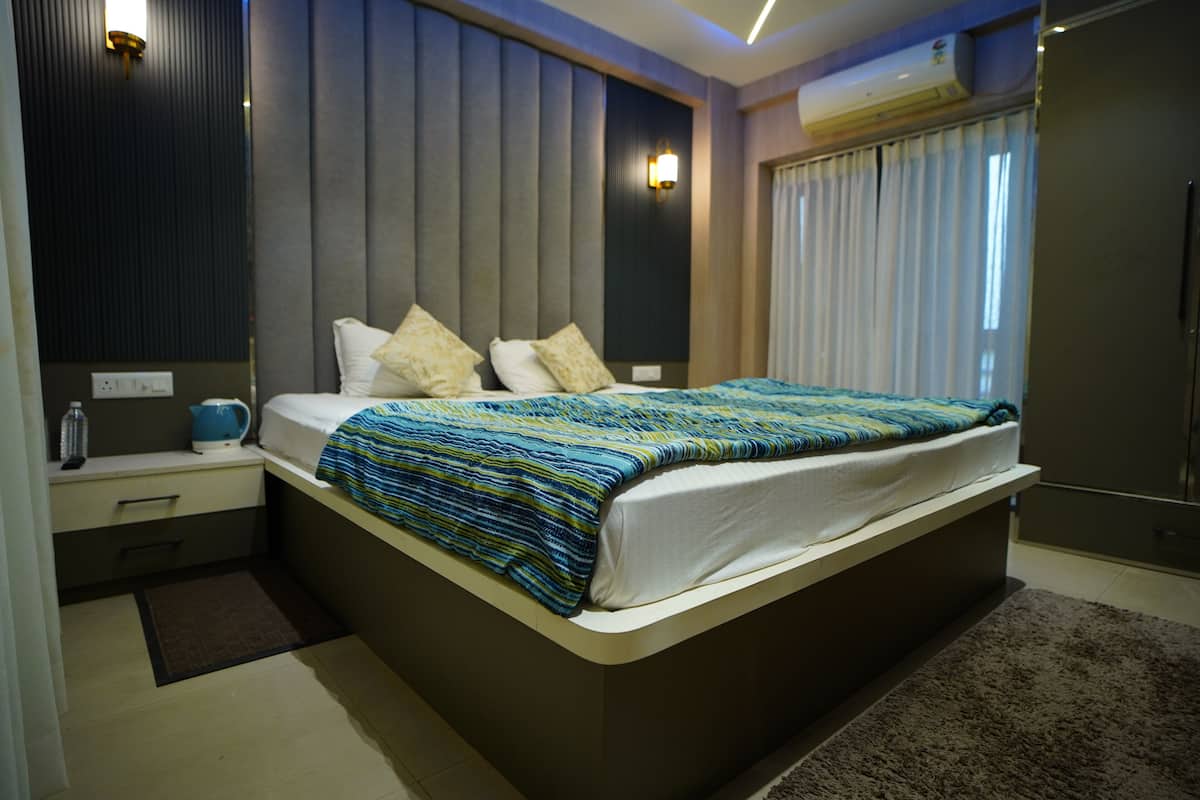 Une chambre moderne avec un grand lit, des tables de chevet, une petite table, une bouteille d’eau et une bouilloire.