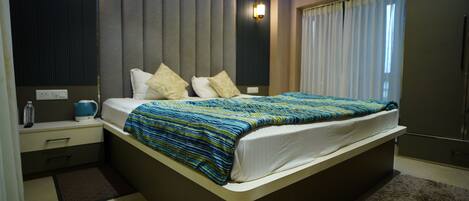 Un dormitorio moderno con una cama grande, mesitas de noche, una lámpara de noche, una botella de agua y un hervidor.