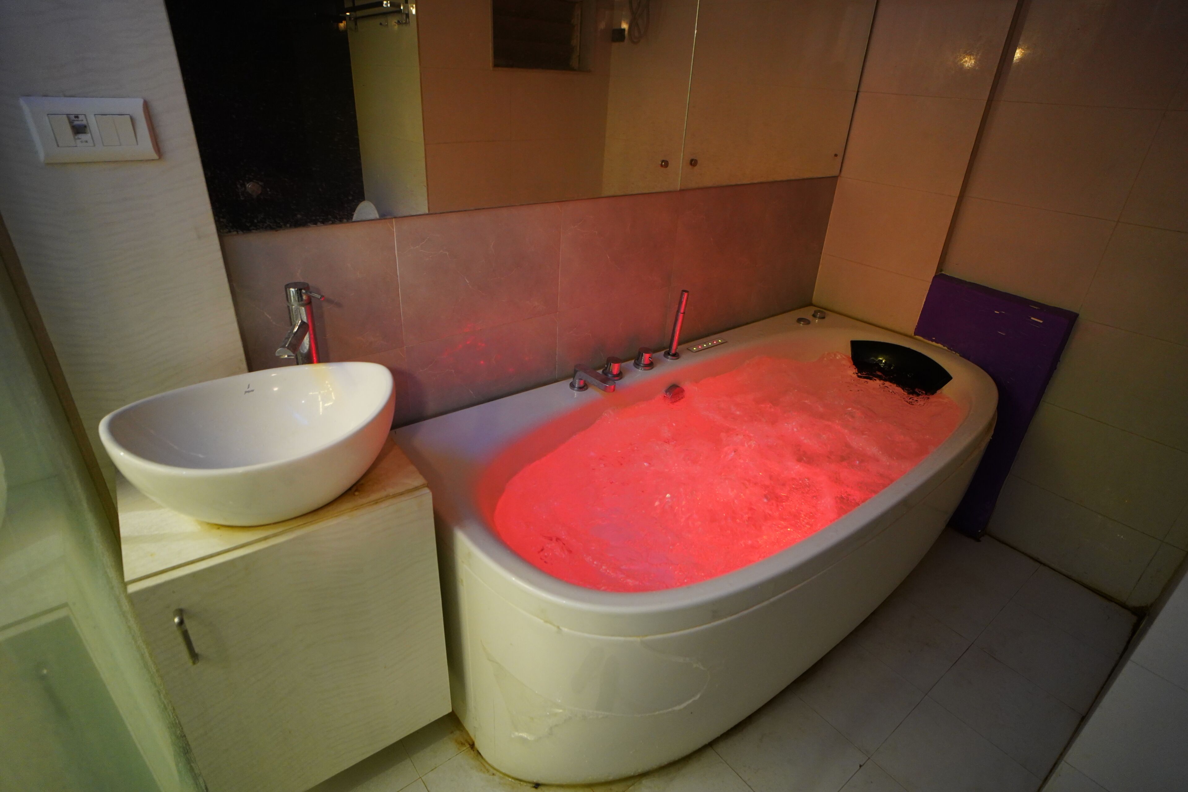 Un baño con un lavamanos blanco, una bañera con iluminación roja y un espejo sobre el lavamanos.