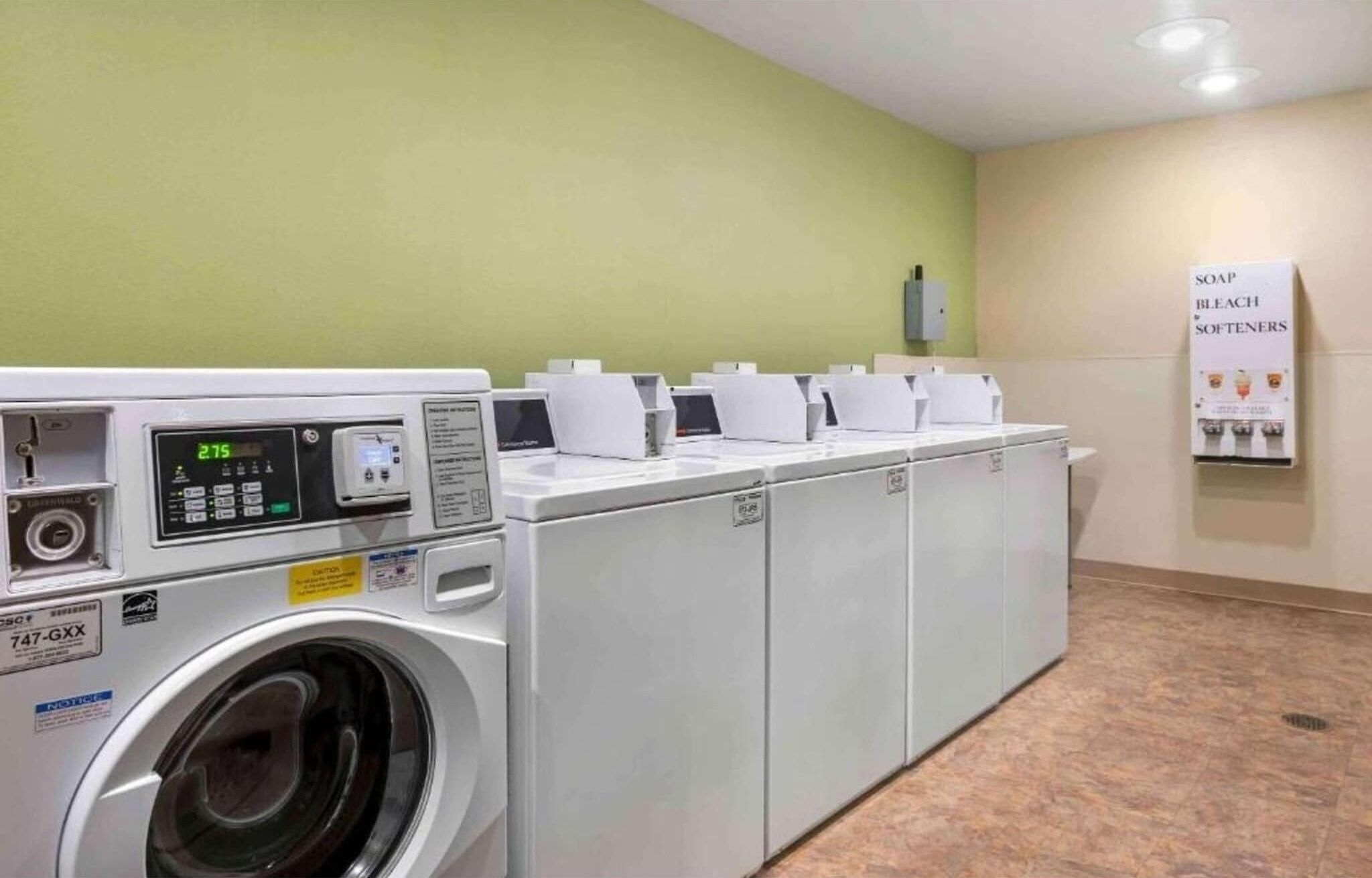 A laundry facility with multiple washing machines and a soap dispenser.
