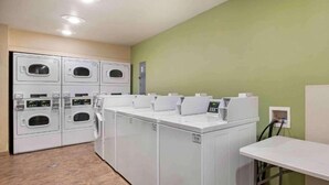 A laundry room with multiple washing machines and dryers, a control panel, and a table.