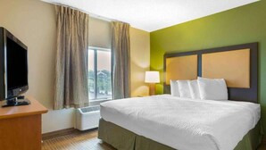 A hotel room with a bed, a television, a window with curtains, a lamp, and a wall heater. - Studio 6 Findlay| Cozy Queen Suite, Nsmk |Kitchen (Findlay OH)