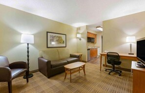 Habitación de hotel con sofá, una mesita, escritorio con silla, televisión y cocina.
