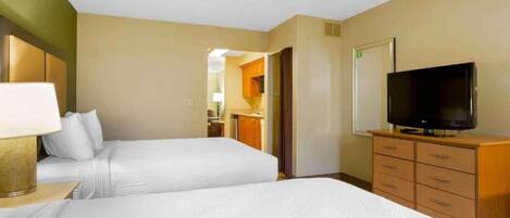 A hotel room with two beds, a television, a desk with a lamp, and a kitchenette.