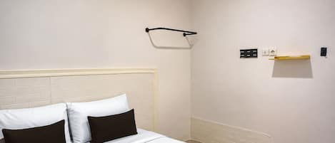 A hotel room with a bed, a headboard, a wall-mounted towel rack, and a small shelf with a light fixture.