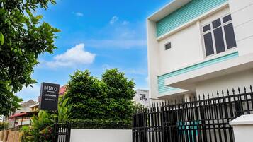 A hotel named 'HOTEL AJRIS HOME' with a signboard, a gated entrance, and a building with a white facade and teal trim.