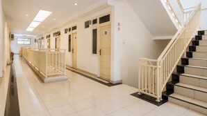A hotel corridor with a staircase on the right, doors with signs, and a tiled floor.