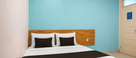Une chambre d’hôtel avec un lit, une tête de lit en bois, un mur bleu et une porte avec une pancarte.