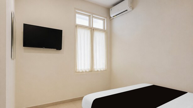 A hotel room with a bed, a television mounted on the wall, and an air conditioning unit.