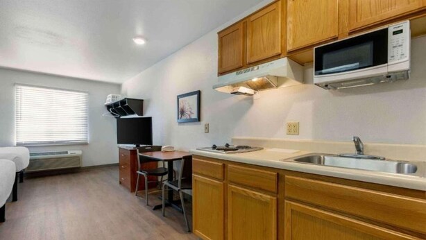 A compact kitchen with wooden cabinets, a microwave, a sink, and a small dining area with a chair and table. - 2 Queen Beds |Non-Smoking, Kitchen (El Paso TX)
