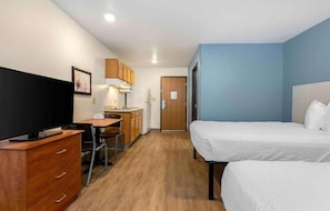 Une chambre d’hôtel de taille réduite, comprenant un lit, un bureau avec une chaise, une télévision et une kitchenette.
