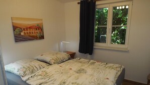 Een slaapkamer met een bed, een nachtkastje, een raam met gordijnen en een schilderij aan de muur.