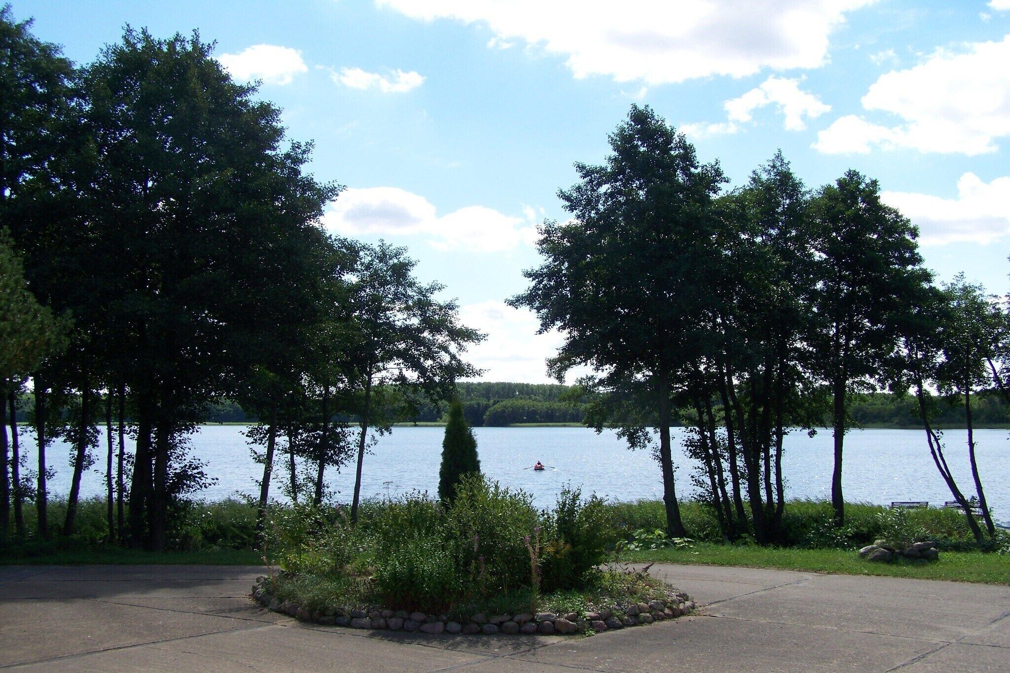 A lakeside view with trees, a clear sky, and a calm body of water.