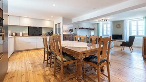 Une cuisine spacieuse équipée d’appareils électroménagers modernes, un coin repas avec des chaises en bois et un salon doté d’une télévision et de sièges confortables.