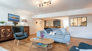 Un salon moderne avec un canapé, un fauteuil, une table basse et, au fond, un coin repas.