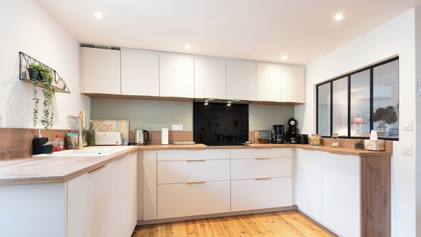 Une cuisine moderne avec des meubles blancs, des plans de travail en bois et une hotte noire.